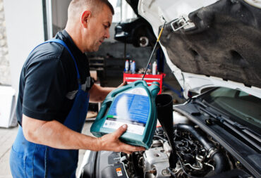 Car repair and maintenance theme. Mechanic in uniform working in auto service, pouring new motor oil.