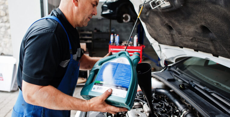 Car repair and maintenance theme. Mechanic in uniform working in auto service, pouring new motor oil.