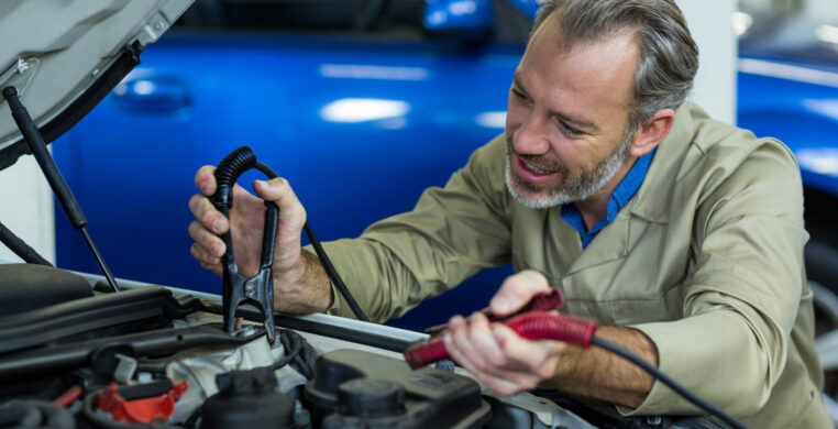 Mechanic attaching jumper cables to car battery in repair garage