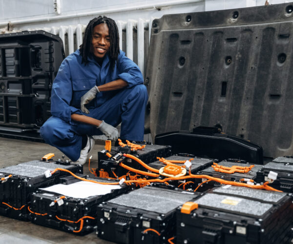 Batteries, electronics of the vehicle. Male mechanic is with car in garage.