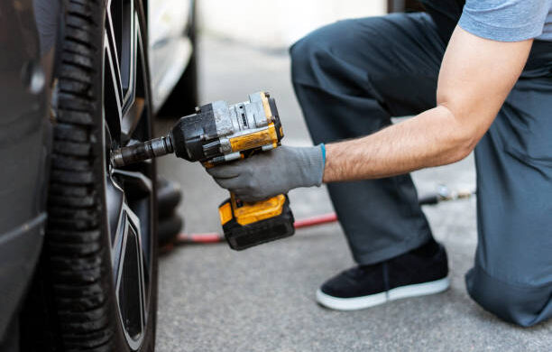 Mechanic is changing a car tire using a battery powered impact wrench in a repair shop