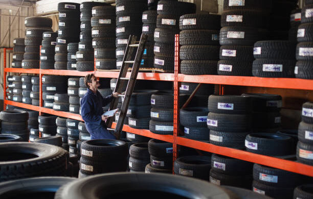 Mechanic holding a new car tire looking upward to shelf of tire inventory to make a vehicle repair in an auto garage