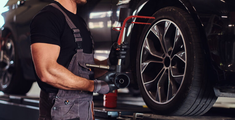 Muscular man is fixing car's wheel with special tool at auto service.
