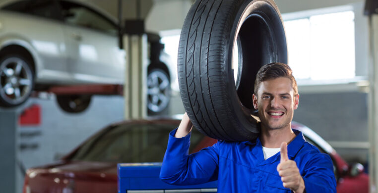 Portrait of mechanic carrying a tyre in repair garage